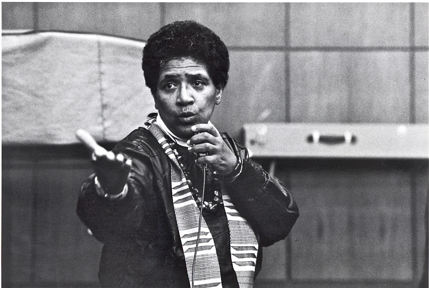 Black and white photo of Audre Lorde talking into a microphone and gesturing with her hand. 