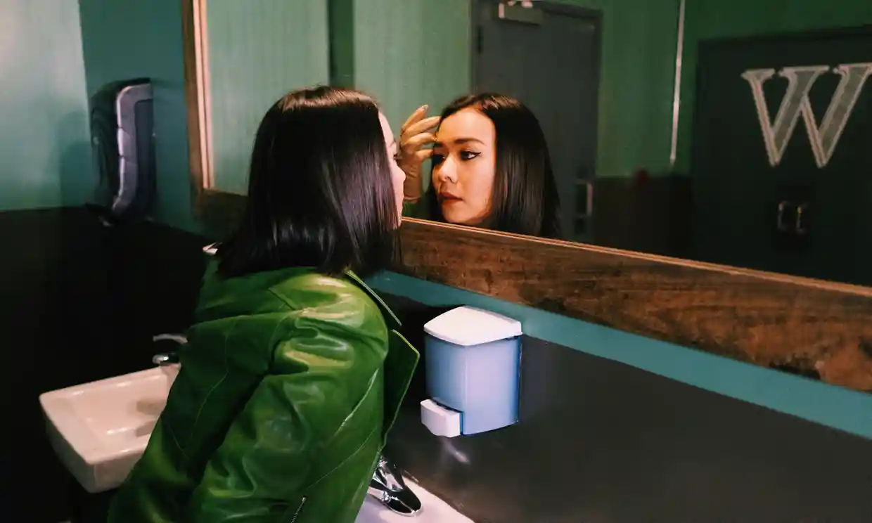 Mitski stares at herself in a bathroom mirror for a photoshoot. (Ngo, Bao. The Guardian. Dec. 2018).