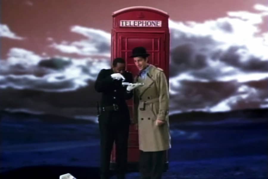 The Inspector and his companion Constable standing outside of a red telephone booth. 