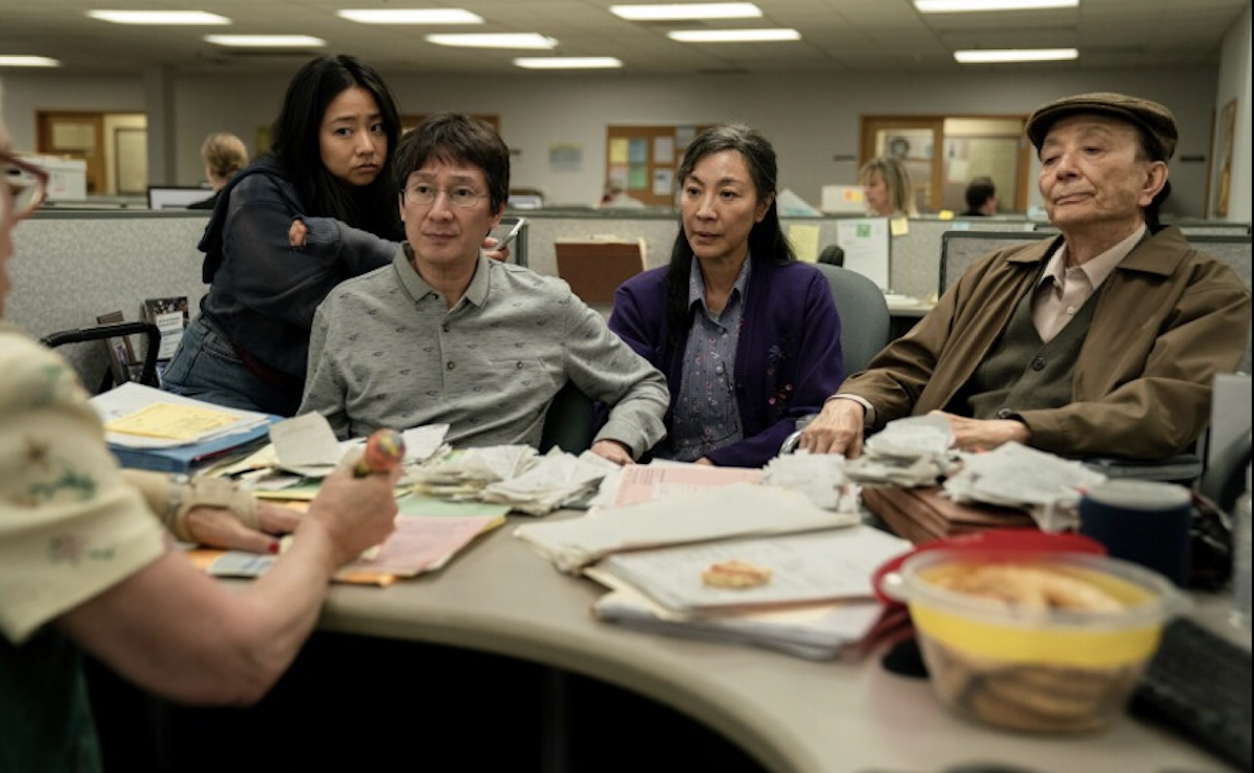 The main cast of Everything Everywhere All At Once -- Joy, Waymond, Evelyn, and Evelyn's father -- sit on the opposite side of a desk at the IRS.