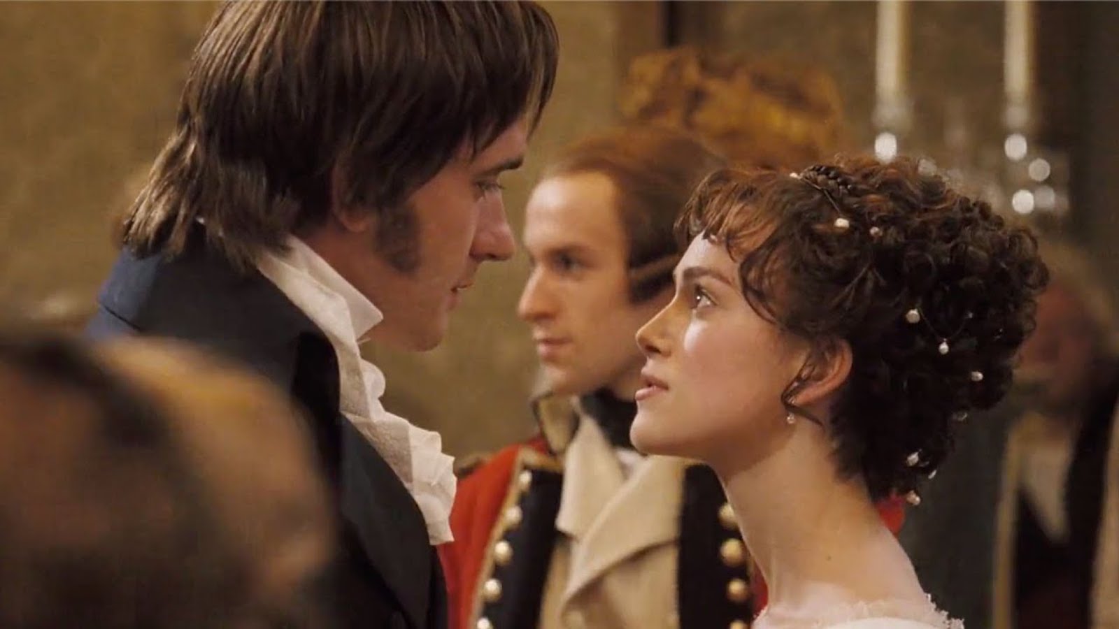 A film still from Pride & Prejudice (2005) shows Elizabeth and Mr. Darcy sizing one another up during a formal dance. Elizabeth glares defiantly up at Mr. Darcy who looks smugly down at her. 