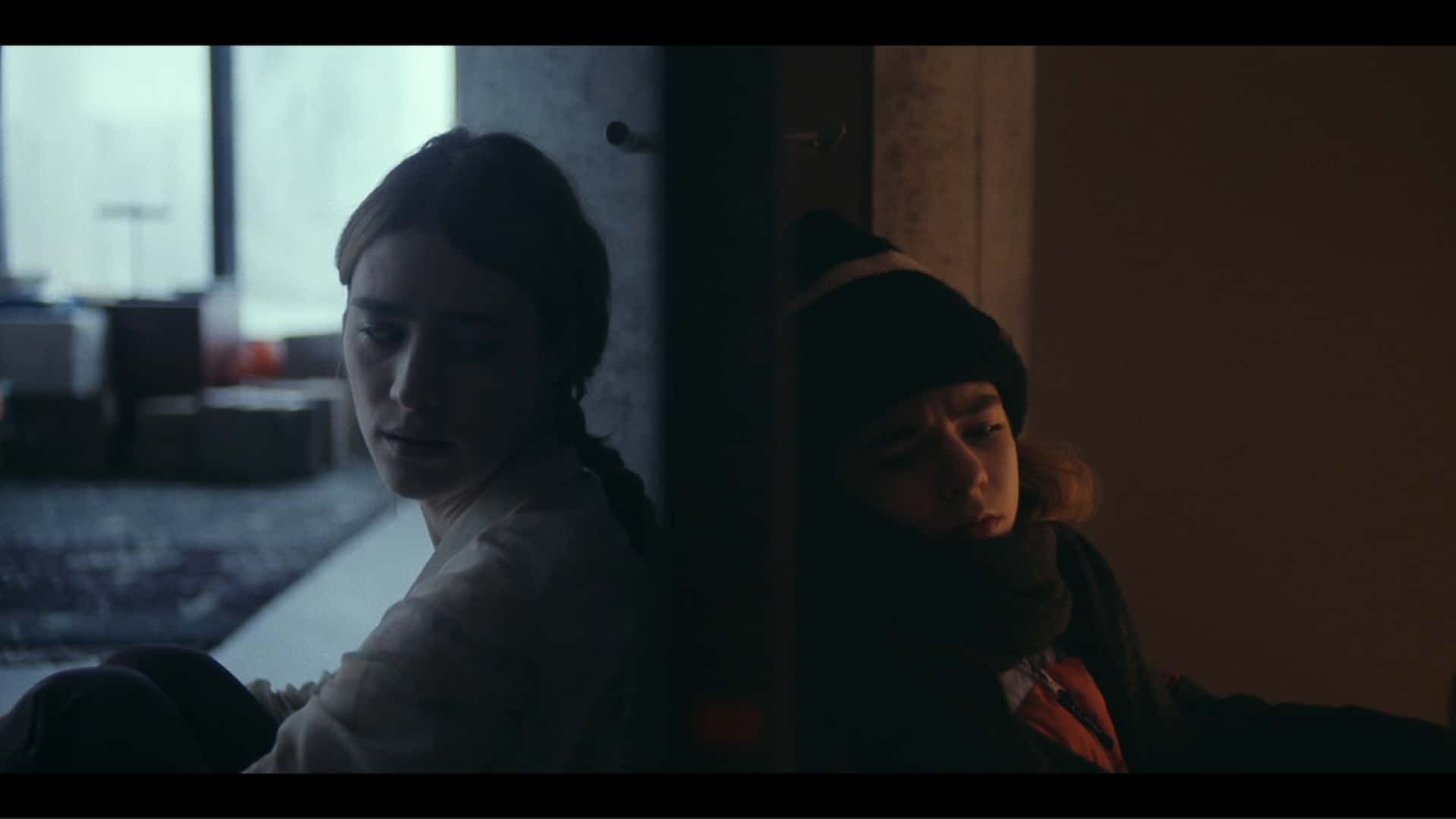 Kirsten (Mackenzie Davis) and Young Kirsten (Matilda Lawler) sit against opposite sides of a closed door.