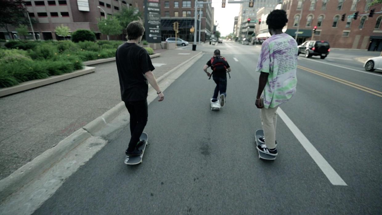 Three men riding skateboards down a fairly busy street in Bing Liu's take on intergenerational trauma narratives.