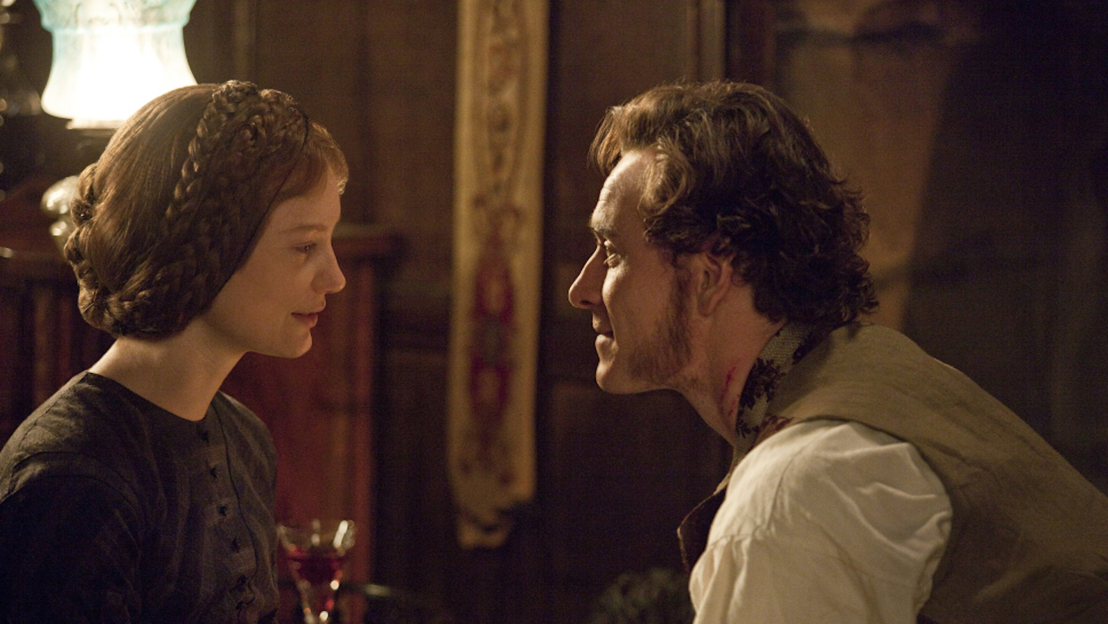 A white man with short facial hair leans in closely to a white woman. Both are dressed in period clothing. They look to be sharing a serious conversation.