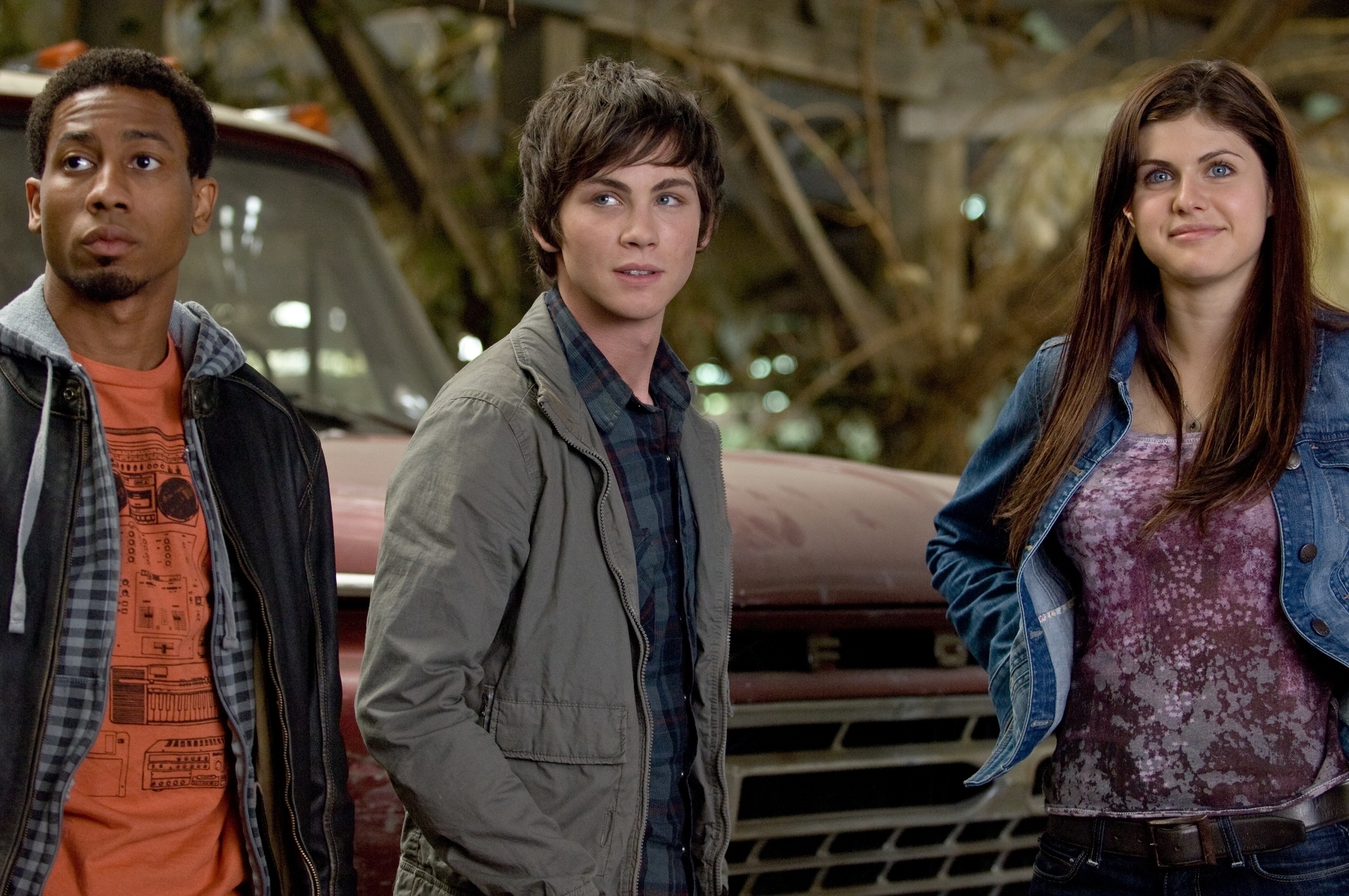 Grover, Percy, and Annabeth stand from left to right in front of an old Fold truck. Grover is a young Black man, Percy is a young white man, and Annabeth is a young white woman. They are dressed in typical mid 2010s fashion.