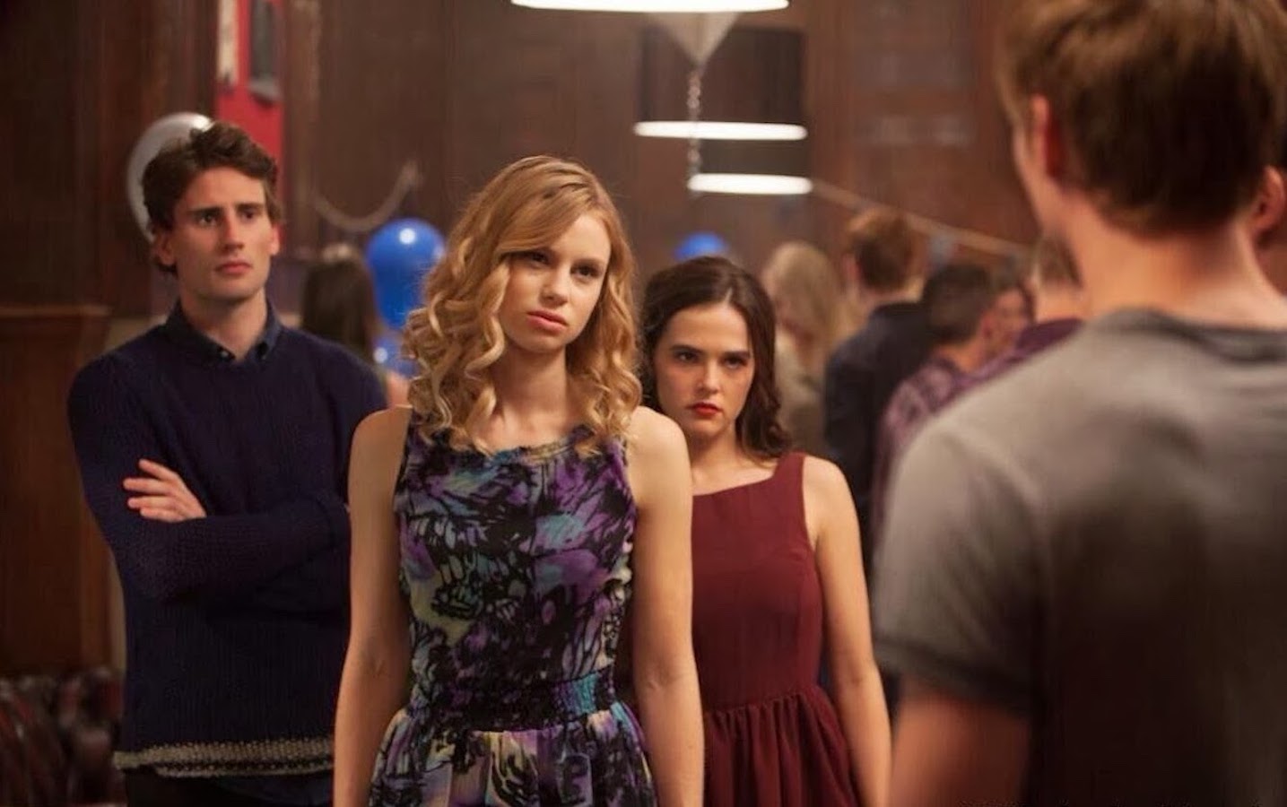 A tall, blonde, white woman stands confrontationally, staring down a man who has his back toward the camera. Behind her stands a shorter, brunette, white woman who glares in the same direction. Behind them both, a tall white man stands with his arms crossed.