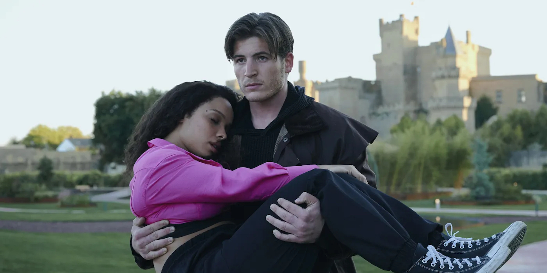 A white man cradles a young Black woman in his arms. She appears to be sleeping or incapacitated. Behind them stands a moderately sized castle.