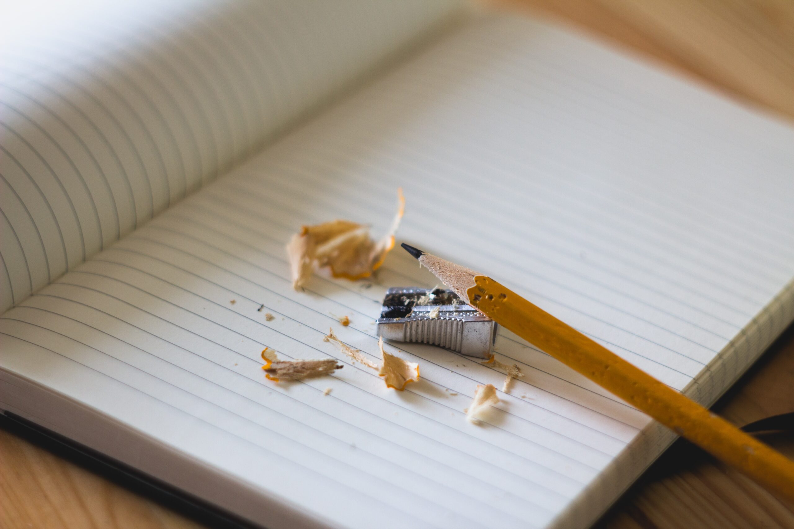 An open lined notebook with a yellow, #2 pencil surrounded by a sharpener and pencil shavings. 