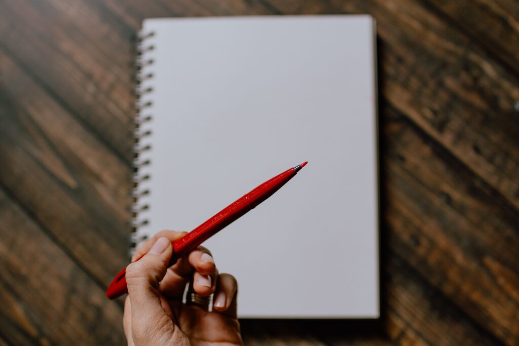 A blank page with a hand holding a felt tip red pen. 