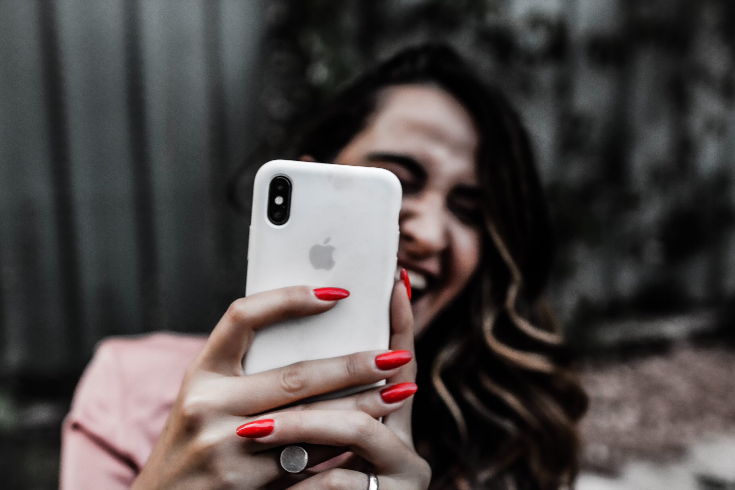 A woman holds her phone to the camera while smiling and laughing. 