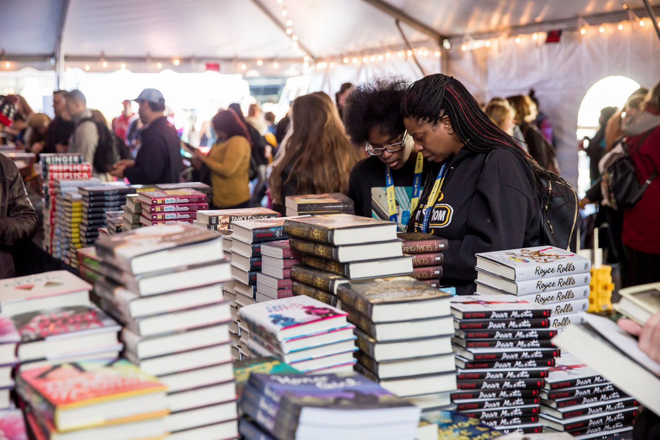Two people browse along a table stacked high with books. Around them, a large crowd of people does the same.