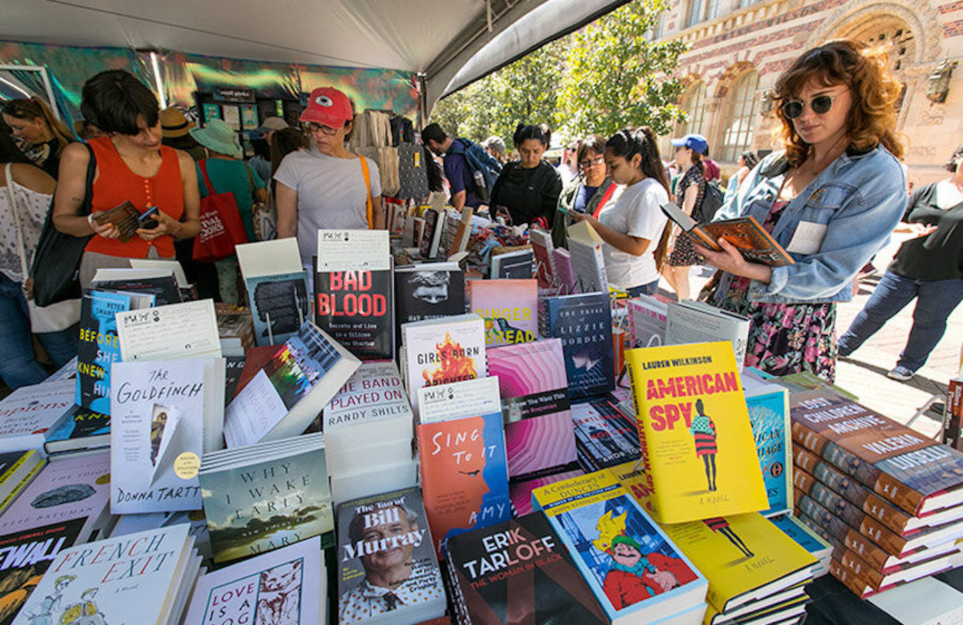 Several young people gather around a massive table where dozens of books are displayed.