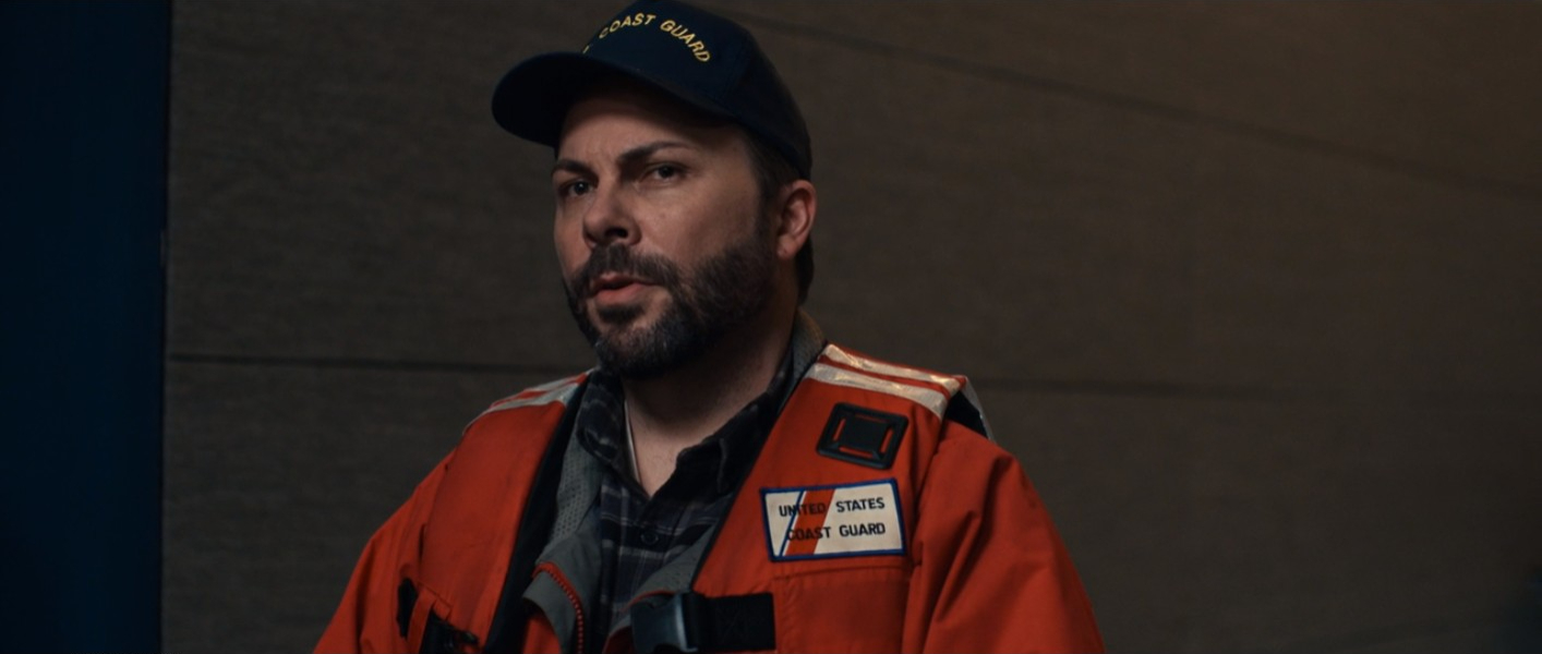 Dale, a Coast Guard officer, standing in the Hawthorn dining room in The Menu (2022).