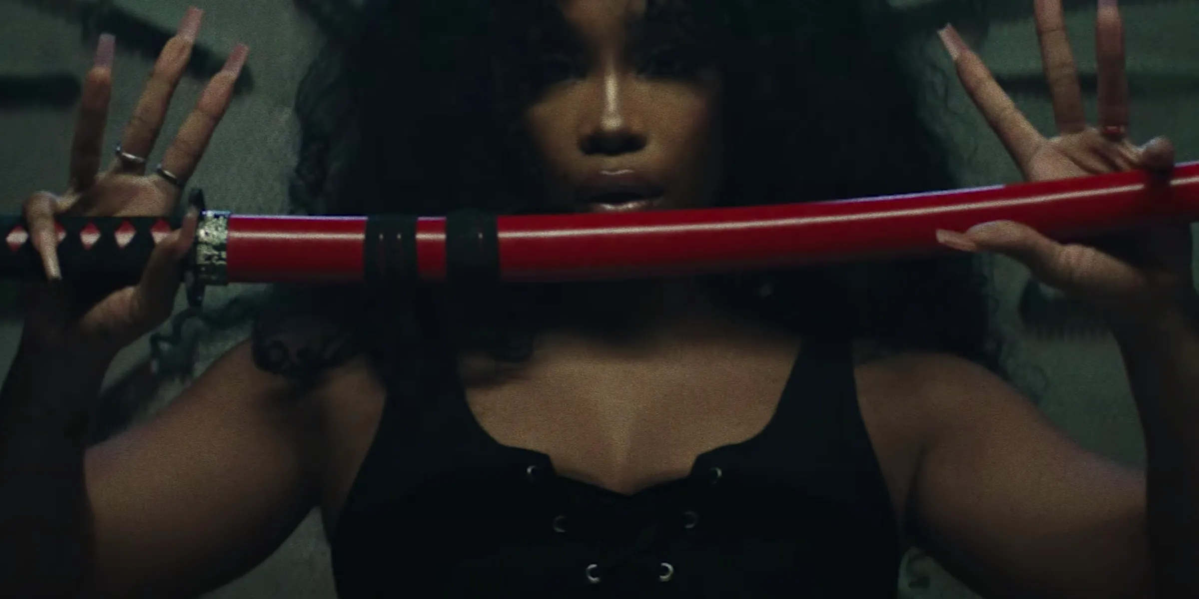 SZA holds a traditional Japanese sword "Katana" at chest height, with her thumb and pinky while her other fingers are held up. 