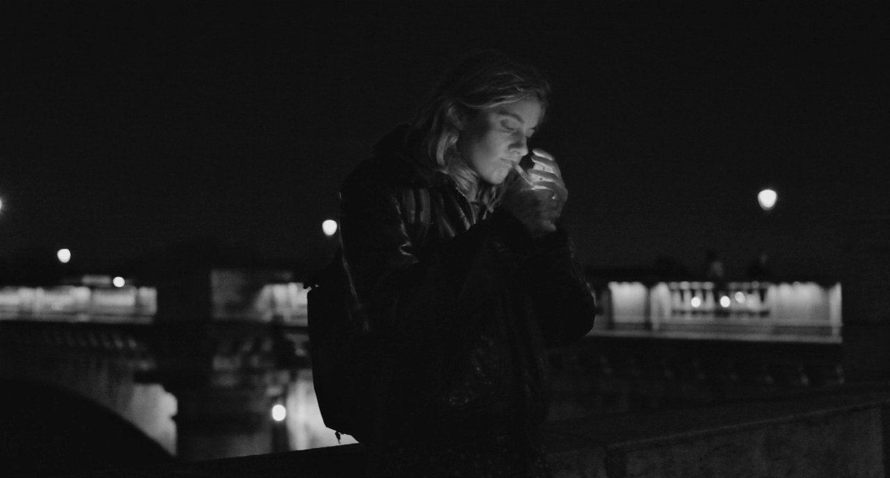 Frances, alone, lighting a cigarette along the Seine in Paris, France. Baumbach, Noah, Dir. Frances Ha. 2012.