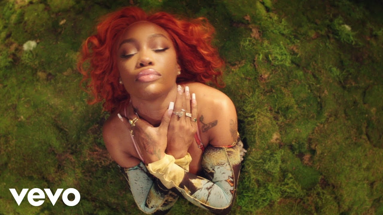 A screenshot from SZA's official music video for "Good Days." A red, curly-haired SZA closes her eyes and arches her neck upwards, her hands in a sort of baptism position. 