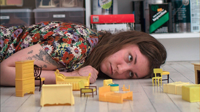 Lena Dunham laying on the floor beside tiny furniture in her movie “Tiny Furniture” (2010).