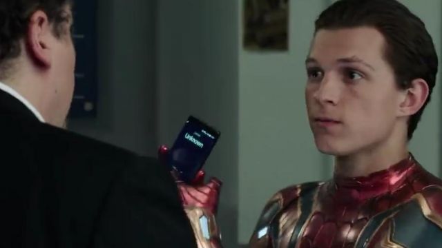Spider-Man (Tom Holland) shows his phone to Happy. 