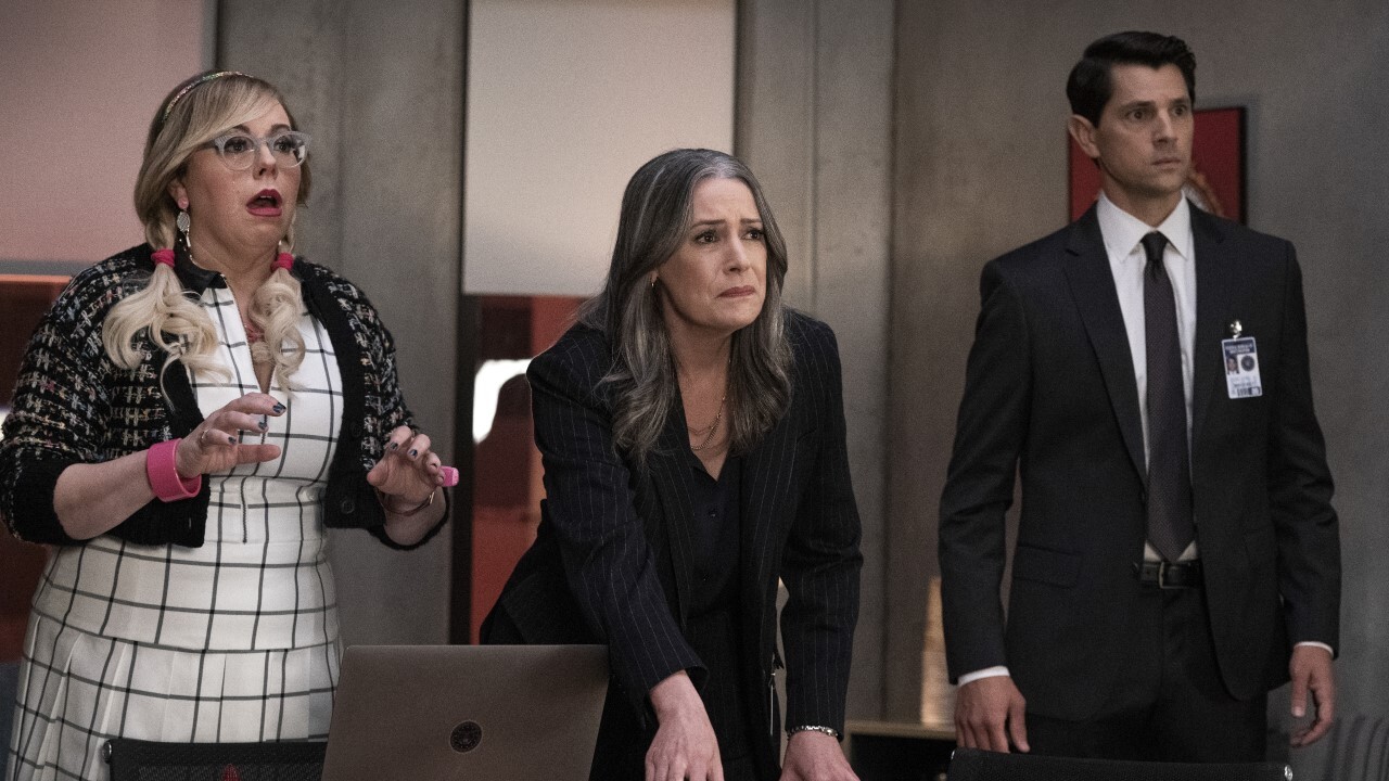 Characters Penelope Garcia, Emily Printess, and Deputy Director Bailey stand around a table looking shocked and distressed. "Criminal Minds." 2005-Present. CBS Studios.