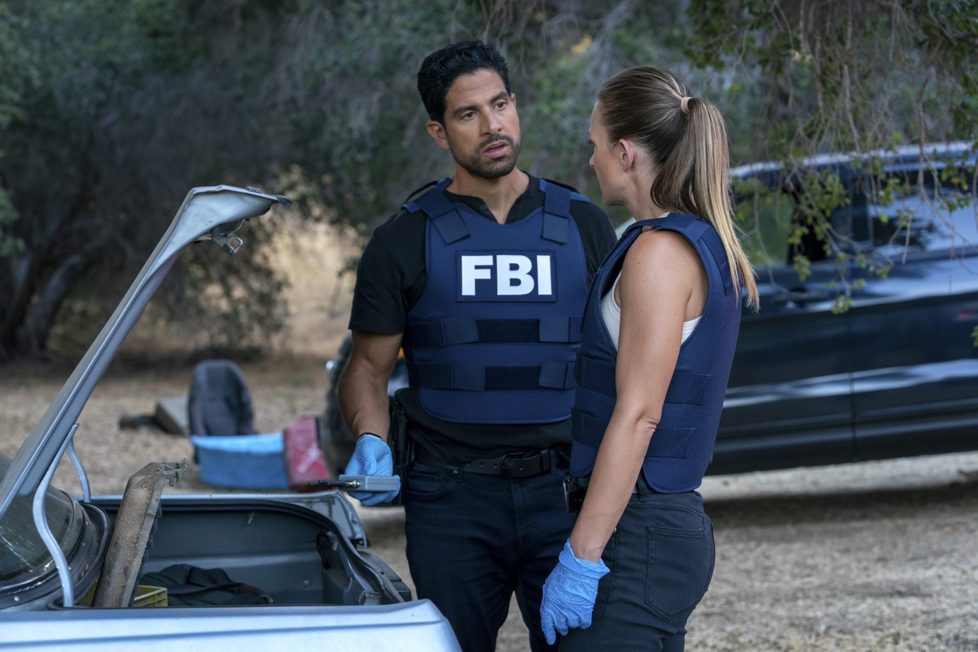 Characters Luke Alvez and JJ Jereau stand on a crime scene, looking through the contents of a "kill kit." "Criminal Minds." 2005-Present. CBS Studios.