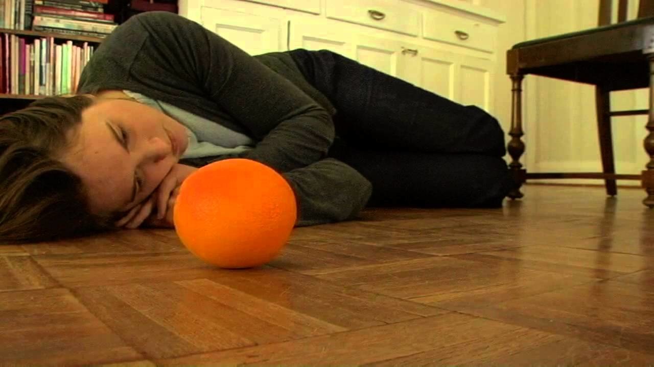 Lori Anne Smithey laying on the floor beside an orange in “I Love You, Apple, I Love You, Orange” (2013).