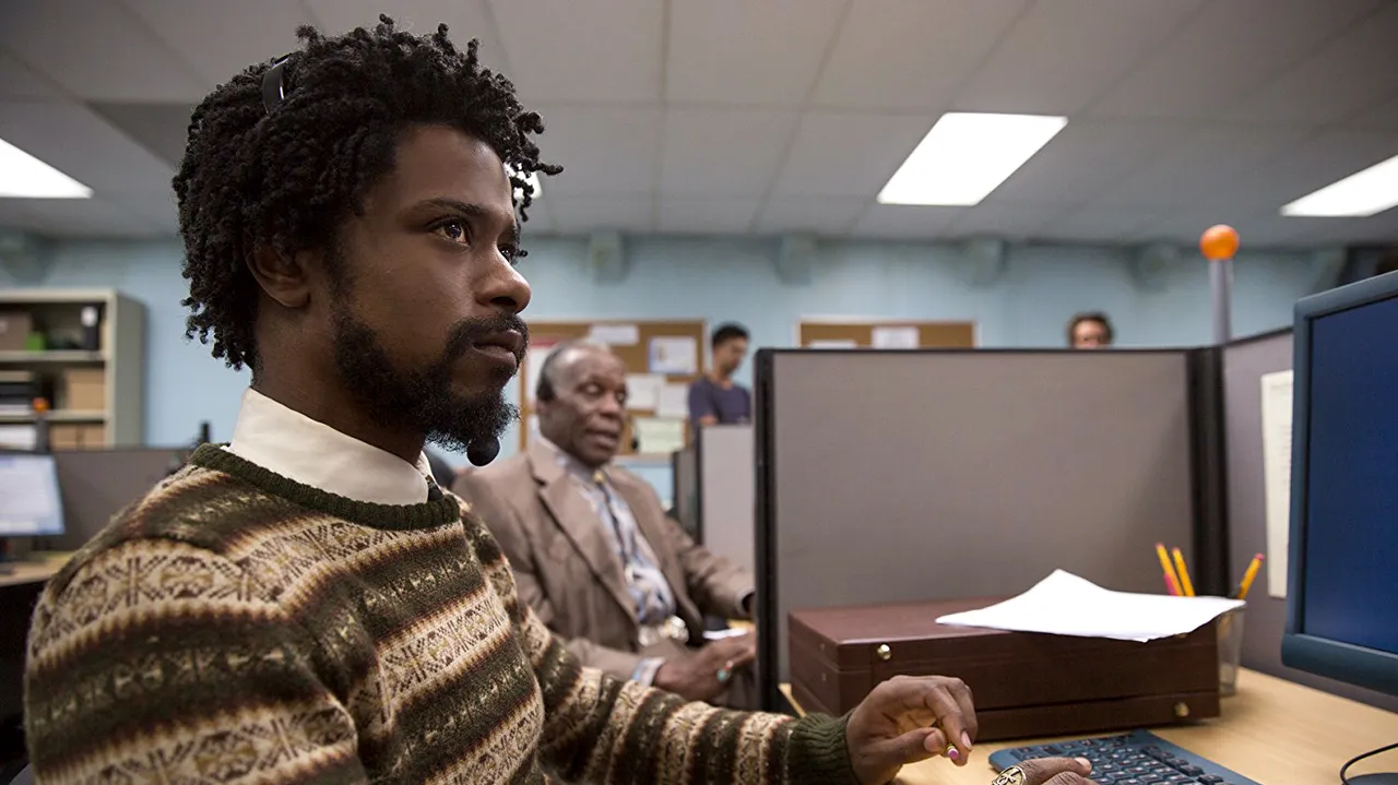 Shot from Sorry to Bother You: Cash sitting in his cubicle at his job