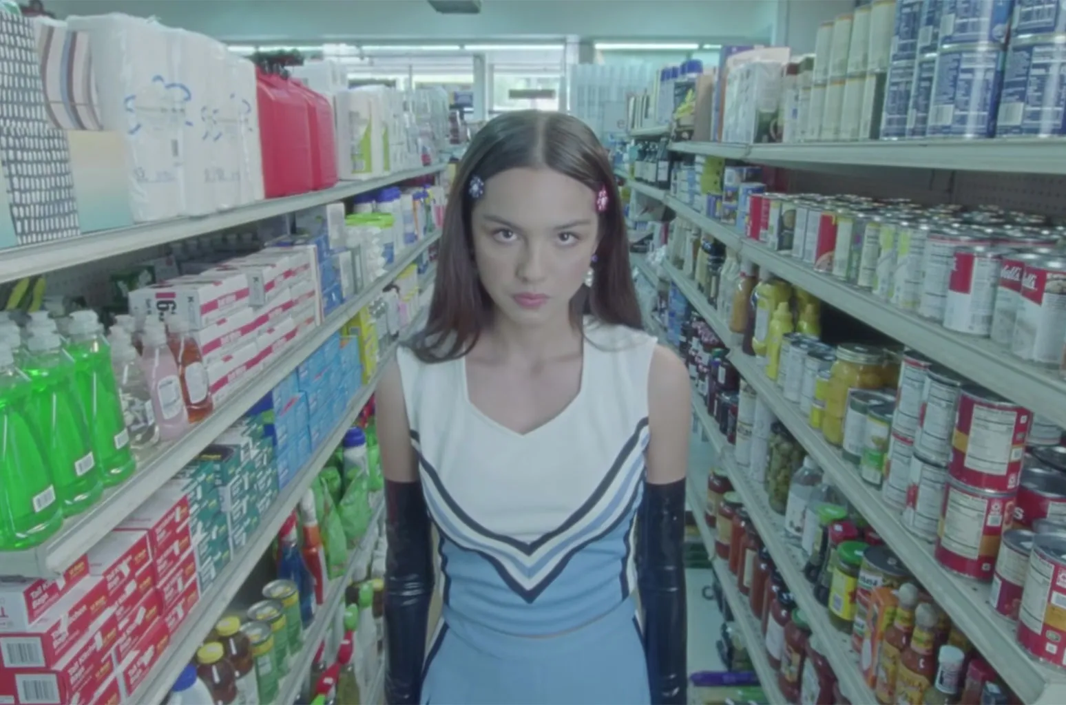 Shot from the "good 4 u" music video: Olivia Rodrigo standing in the drugstore, wearing a cheerleading uniform.