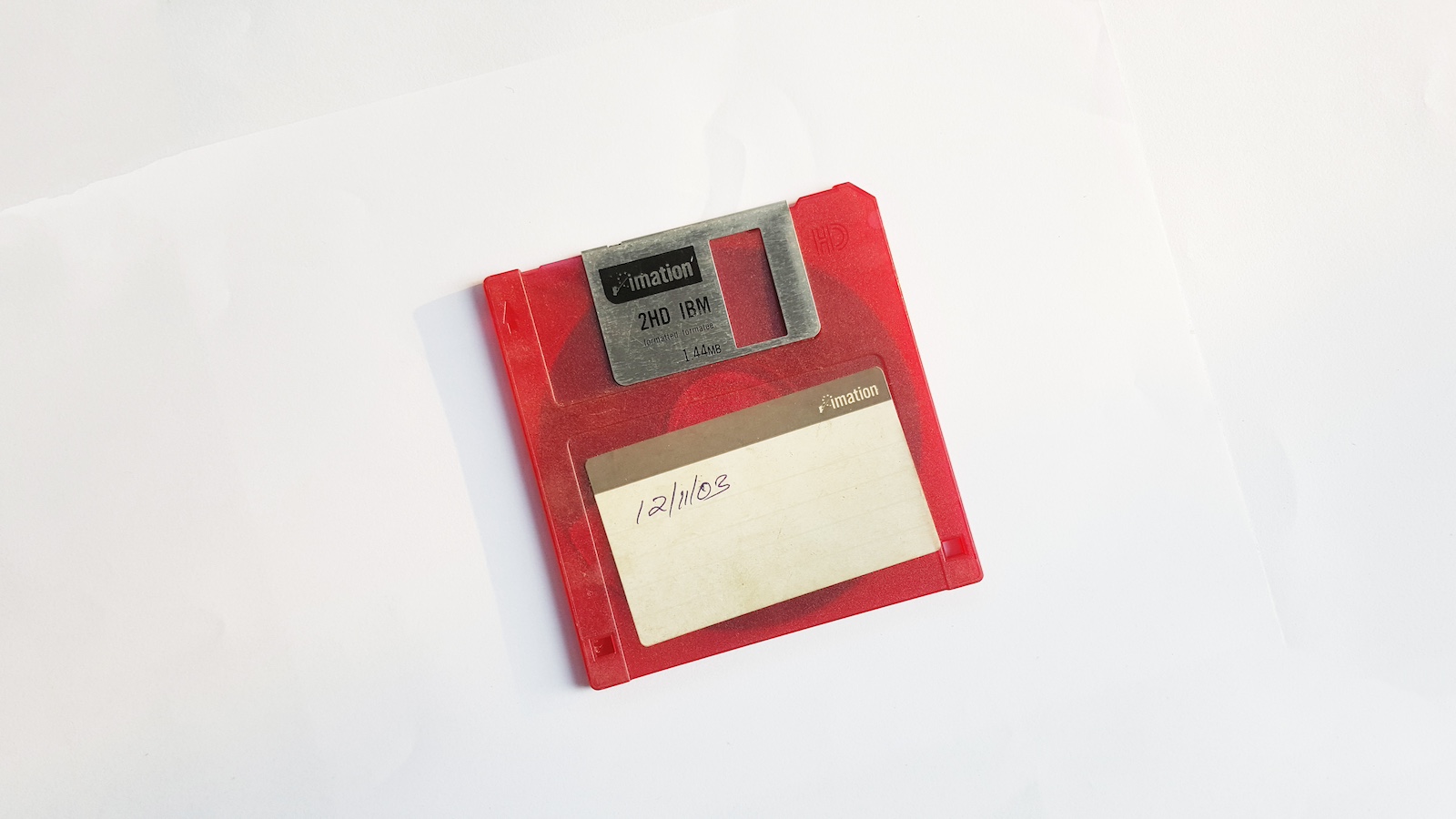 A red and white floppy disk lays on a white surface.