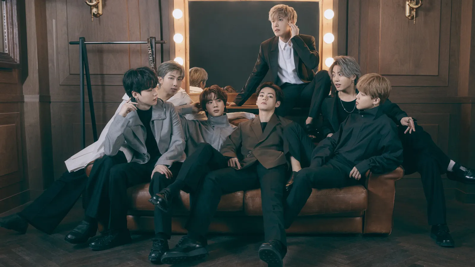 BTS members RM, Suga, V, J-Hope, Jungkook, Jimin, and Jin sitting on a couch.