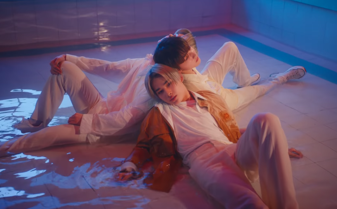 ENHYPEN member Ni-Ki leans against his group members on the floor.