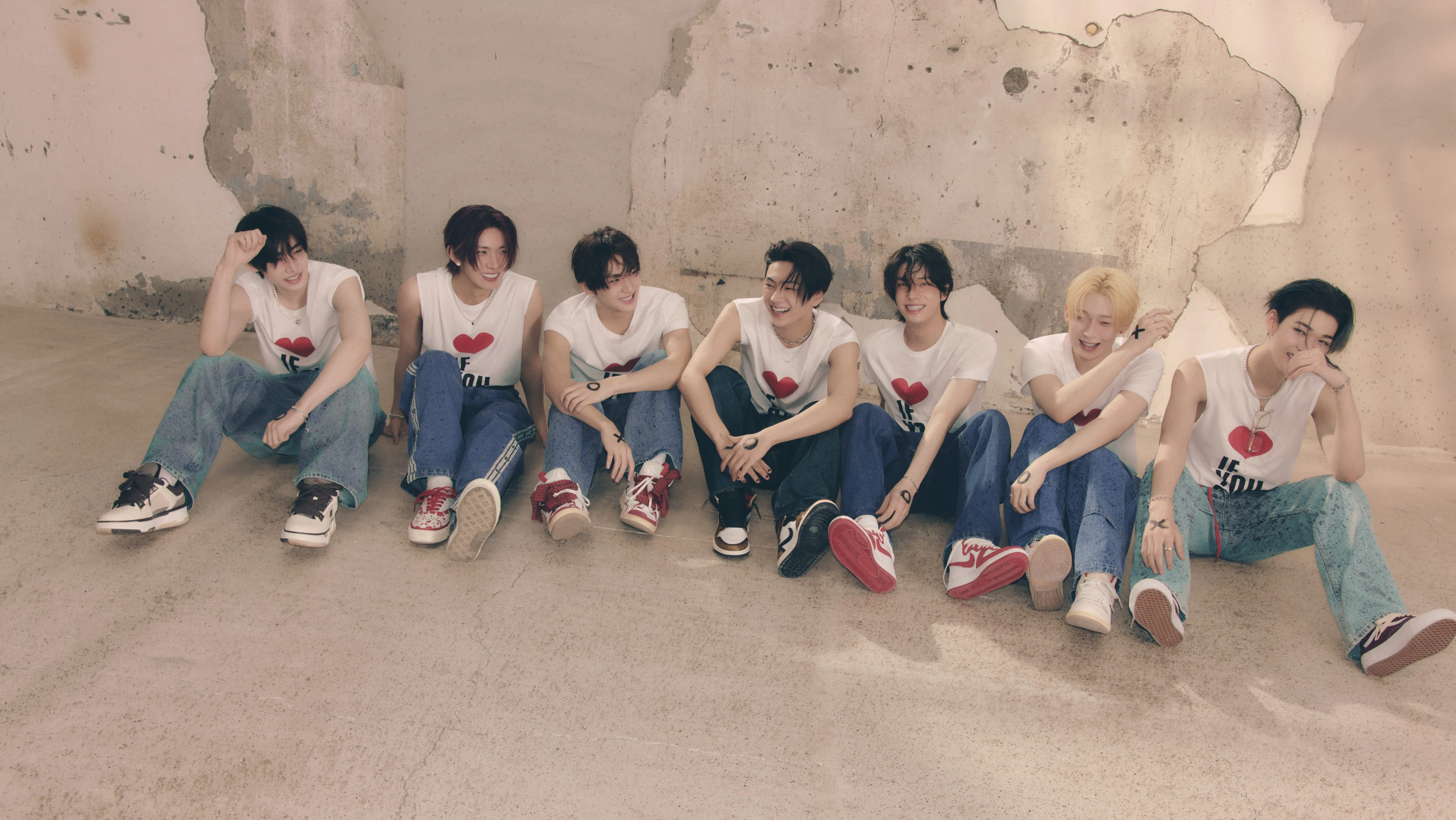 ENHYPEN members Sunghoon, Heeseung, Jungwoo, Jay, Jake, Sunoo, and Ni-Ki sitting down, smiling.