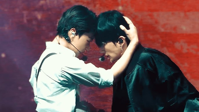ATEEZ members Woosung and San touching foreheads during a performance.