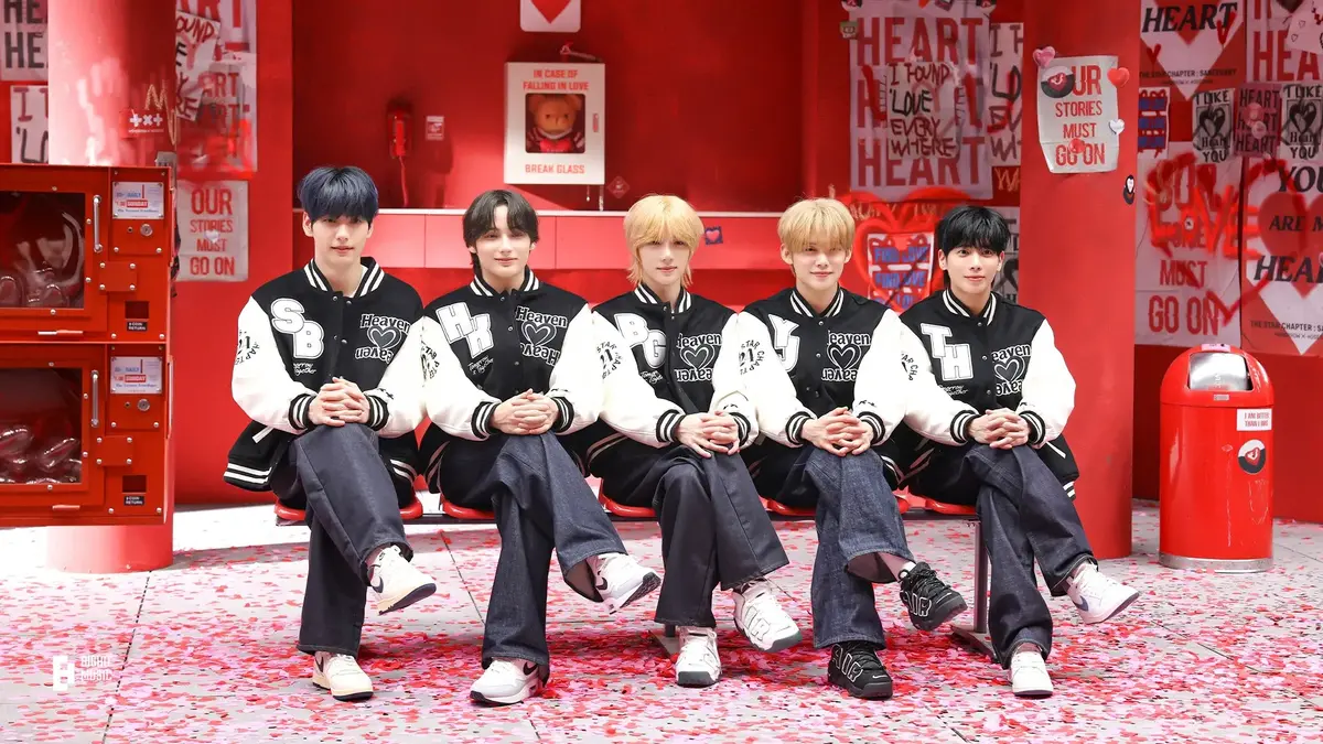 Tomorrow By Together members Soobin, Hueningkai, Beomgyu, Yeonjun, and Taehyon sitting on a bench with their legs crossed.