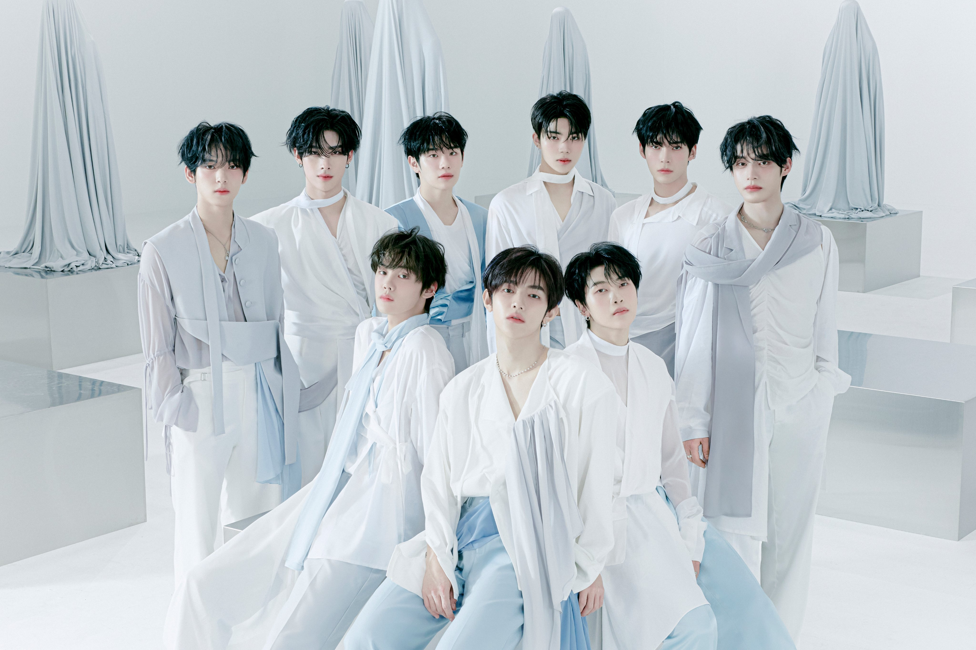 ZERBOBASEONE members Zhang Hao, Ricky, Tarae, Gunwook, Gyuvin, Jiwoong, Hanbin, Matthew, and Yujin where white and blue outfits while looking at the camera.