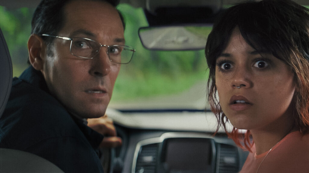 Elliot (Paul Rudd) and Ridley (Jenna Ortega) sit in a car, shockingly staring at something. Scharfman, Alex. Death of a Unicorn. 2025.