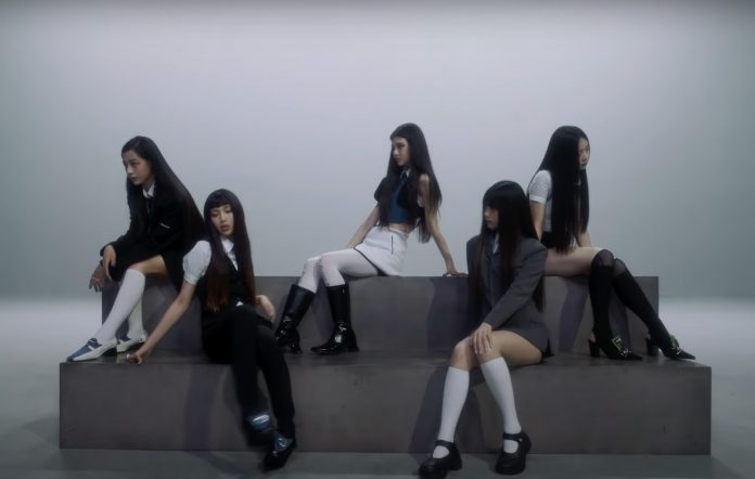 NewJeans members Danielle, Hyein, Haerin, Hanni, and Minji sit on steps.