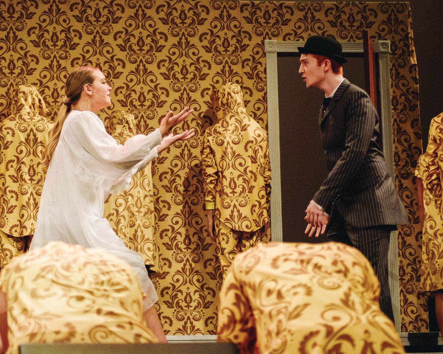 A play for "The Yellow Wallpaper" from 2018. A woman in a white gown is rushing to the man in a suit, they appear to be arguing. The infamous yellow wallpaper surrounds the set with many people dressed in the pattern of the wallpaper in order to personify the setting.

Buglewicz, Trent; Robson, Lex. The Yellow Wallpaper. Lin-Mar High School choir, 2018.