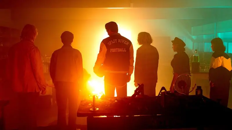 School Spirits characters in colorful lighting with their backs to the camera.