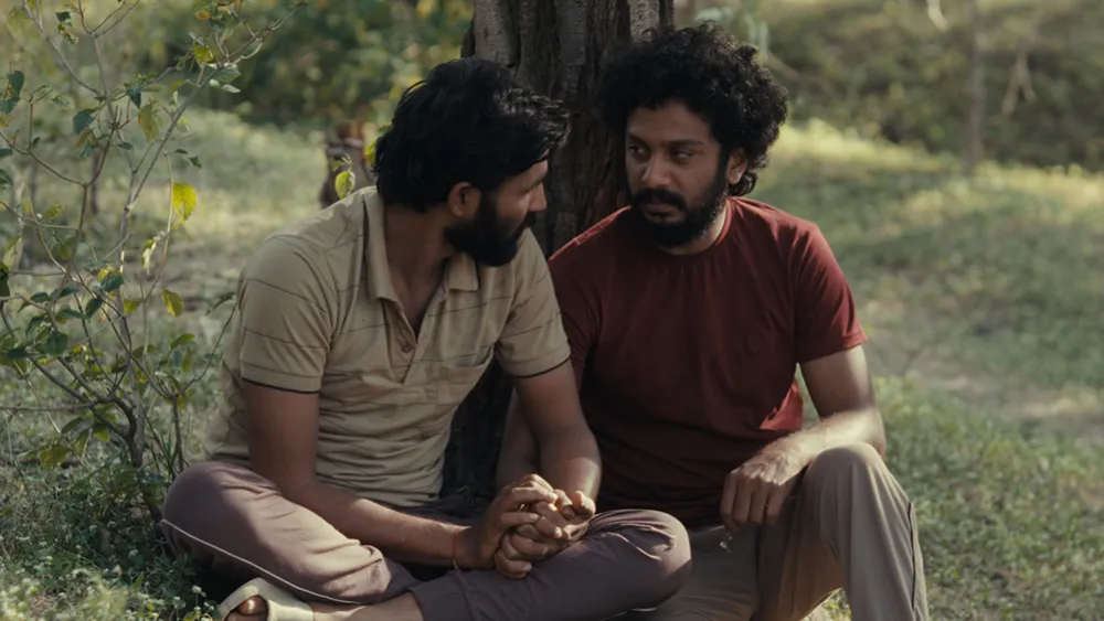 Balya (Suraaj Suman) and Anand (Bhushaan Manoj), sitting together under a tree. Their hands are clasped together and they are looking into each others eyes.