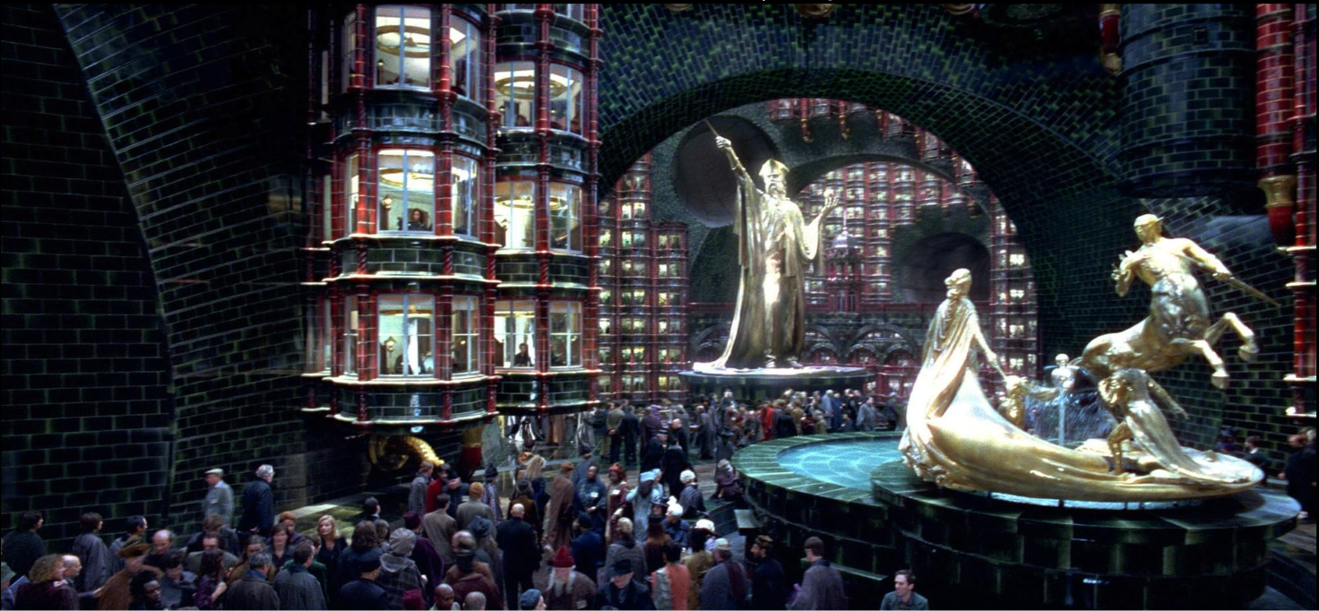 The main floor of the Ministry of Magic, prominently featuring a male wizard statue, and and a statue of a witch and other magical beings below it.
