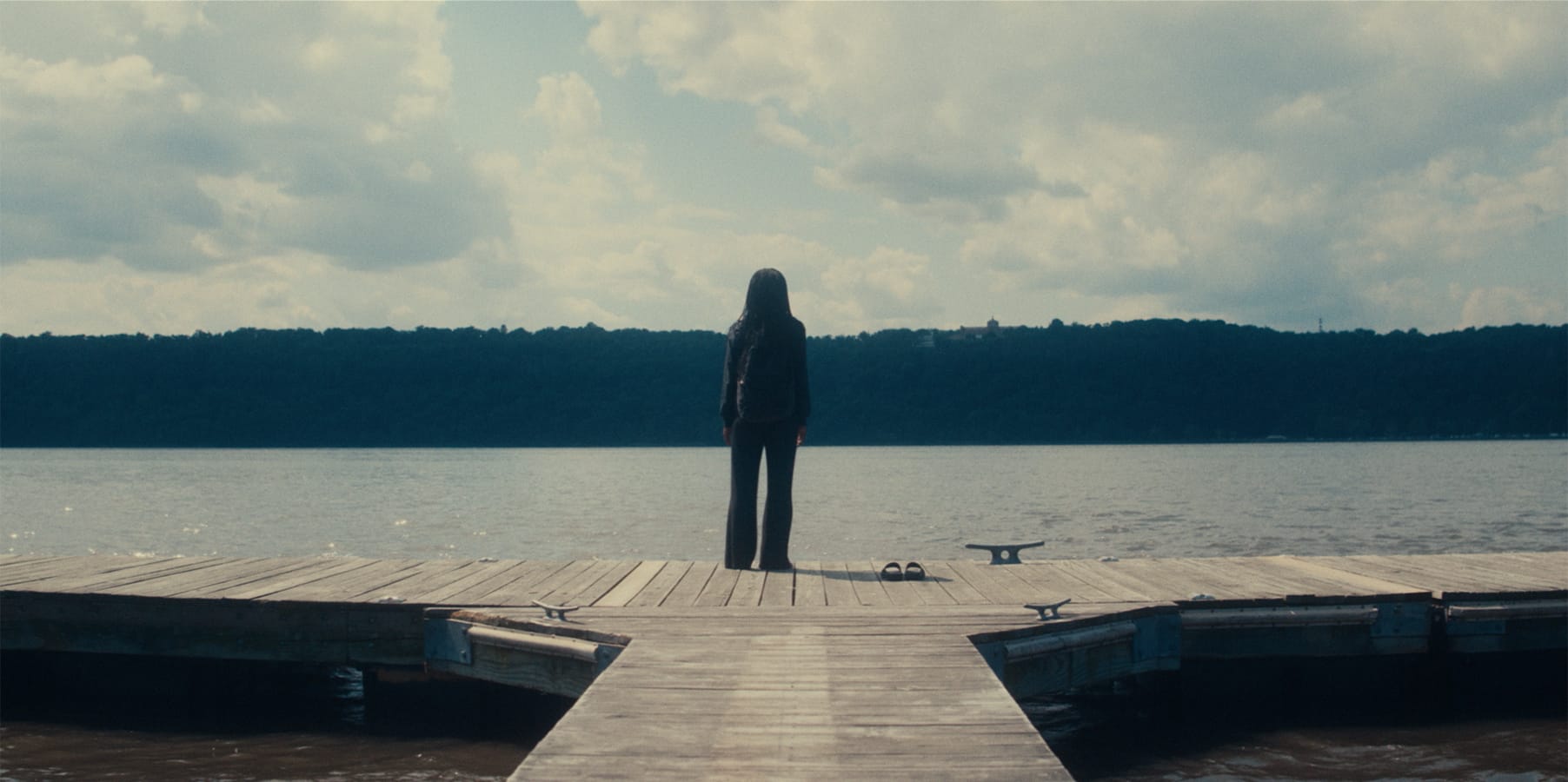 Still from Nanny, Aisha stands on a dock on the lake. She stares off at the water.