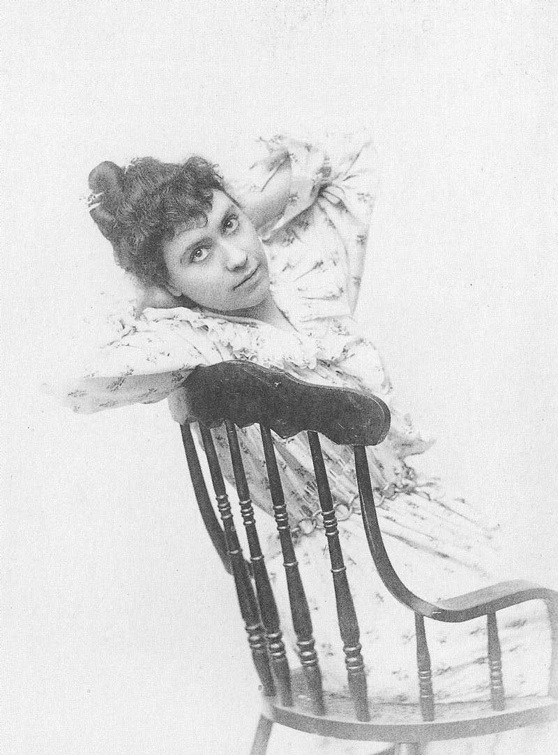 Ada Dwyer Russell posed in a wooden chair with her hands behind her head, gazing just above the camera.