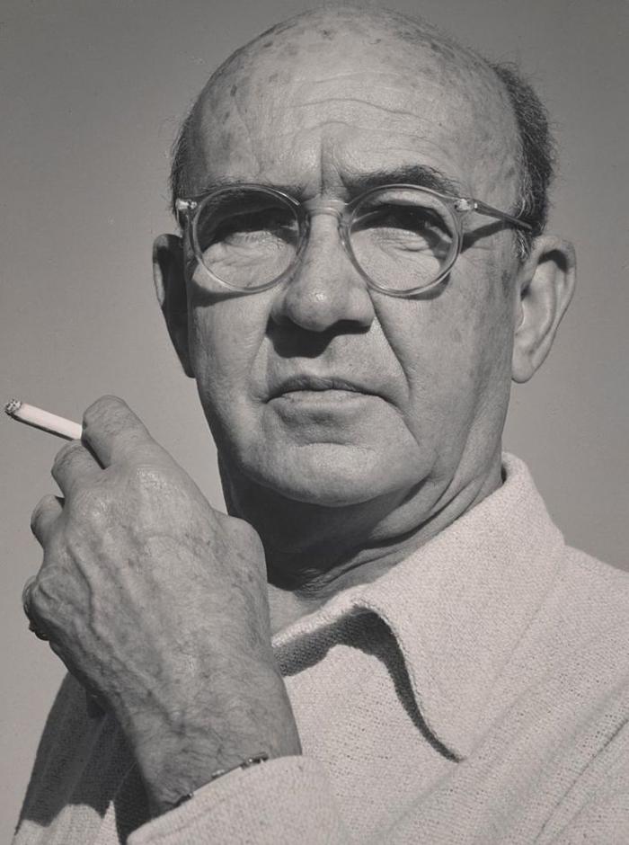 Author Witter Bynner stares just beyond the camera. He is wearing glasses and is holding a cigarette in one hand.