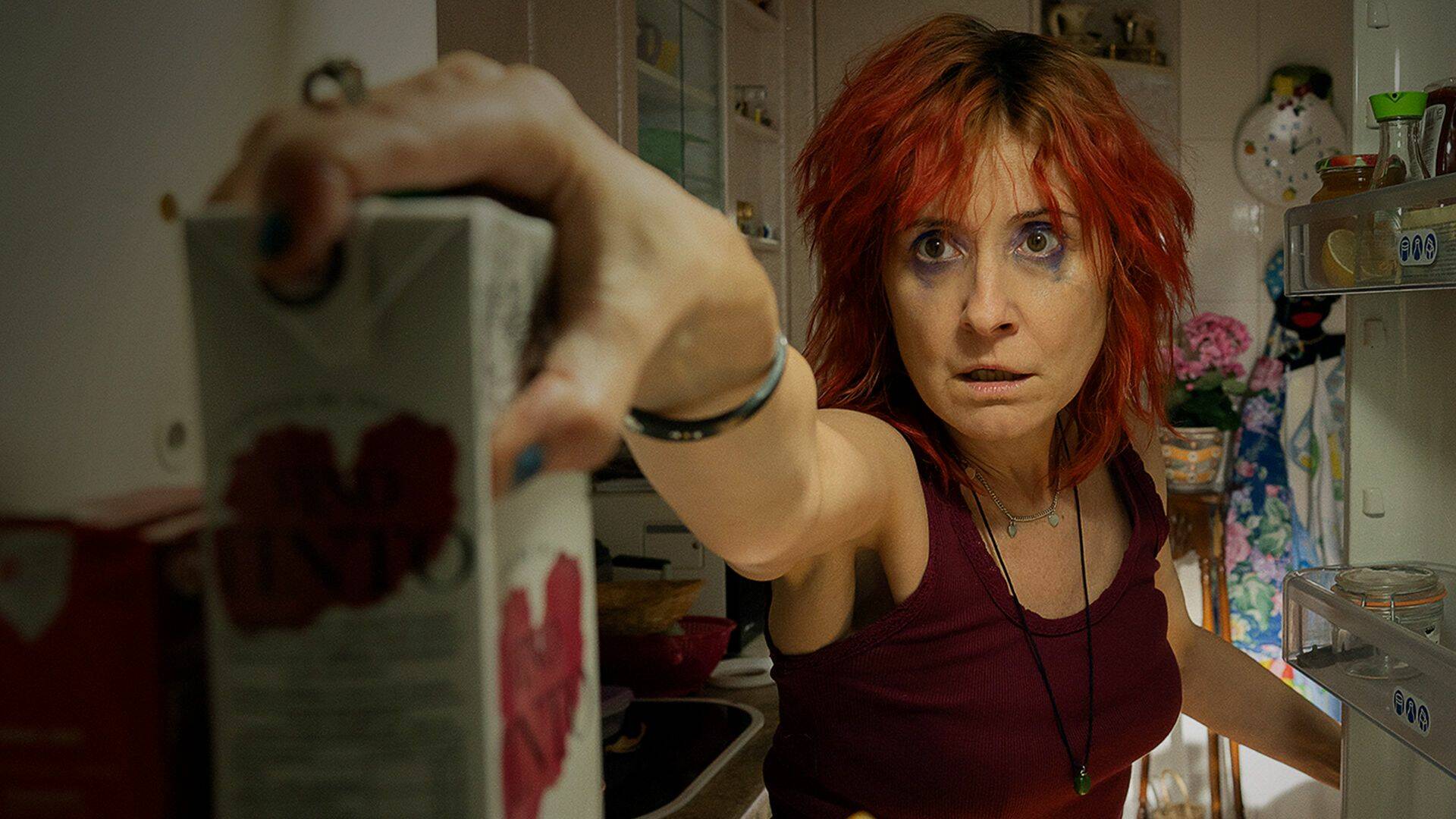 Adela grabs a drink from her fridge. 