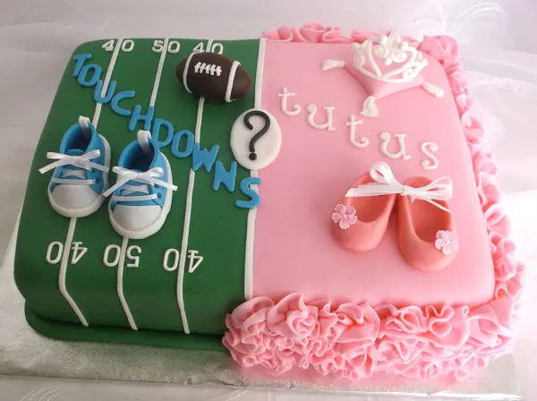 A gender reveal cake saying "touchdowns or tutus?" The touchdown half is a football field with blue shoes and the tutus side sis ruffly pink with a white crown.