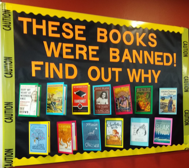 A wall that has thirteen books displayed with a sign saying "these books were banned, find out why."