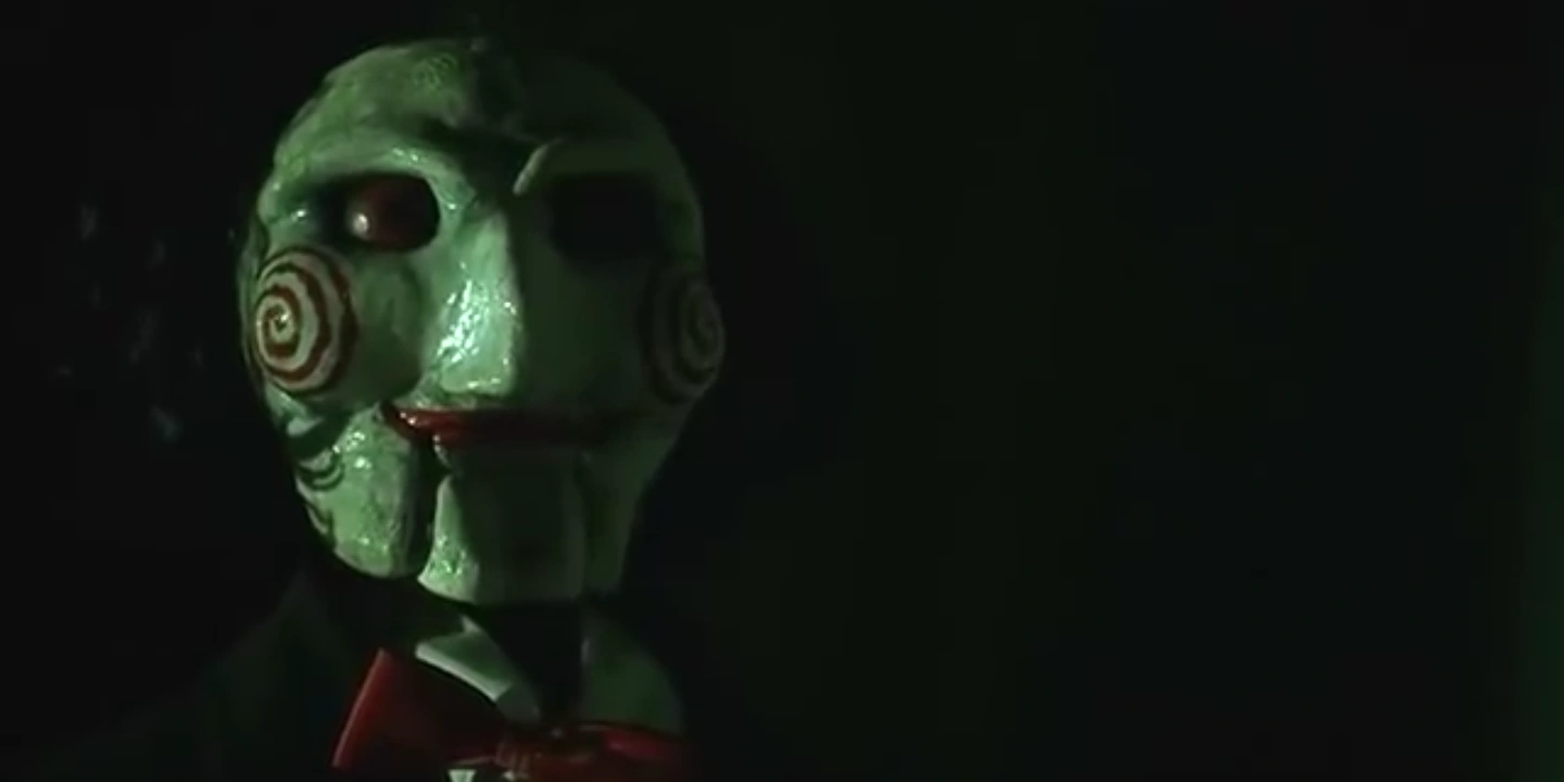A close-up of Billy the Puppet with green lighting. Wan, James, dir. Saw, 2004.