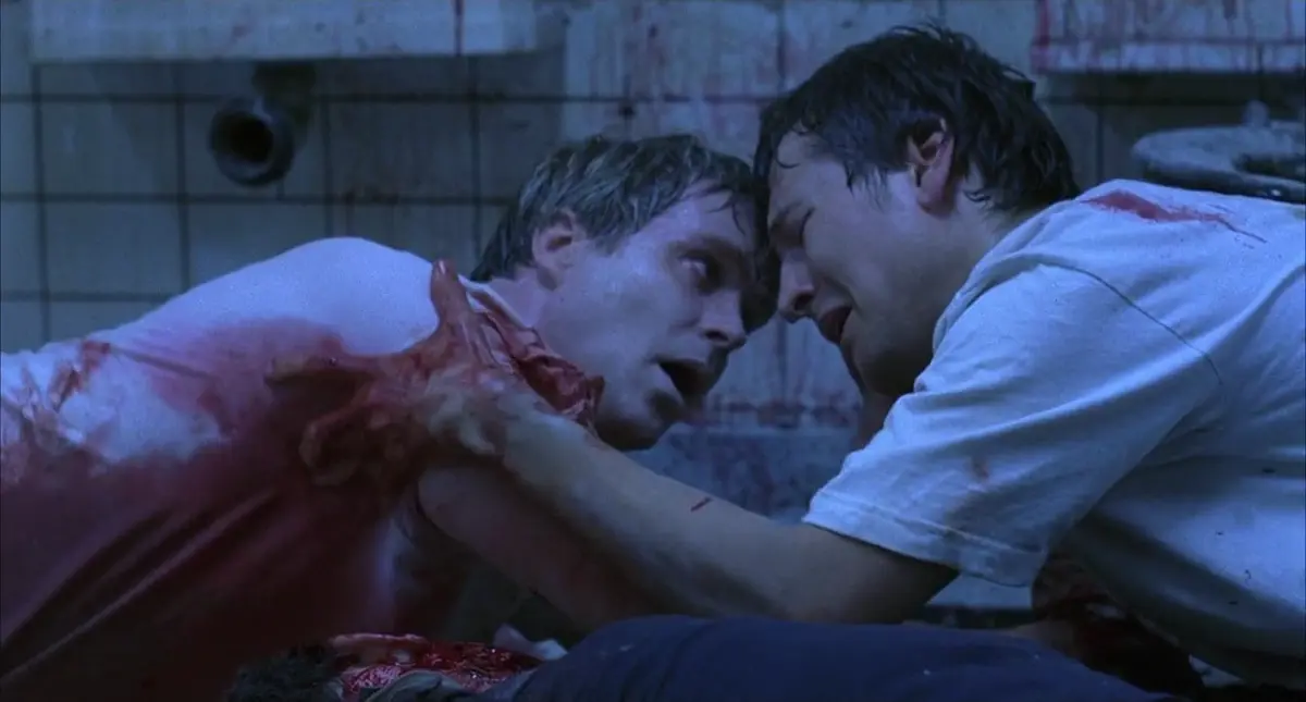 Adam Stanheight, played by Leigh Whannell, holds on to a bloodied Lawrence Gordon, played by Cary Elwes. Wan, James, dir. Saw, 2004.