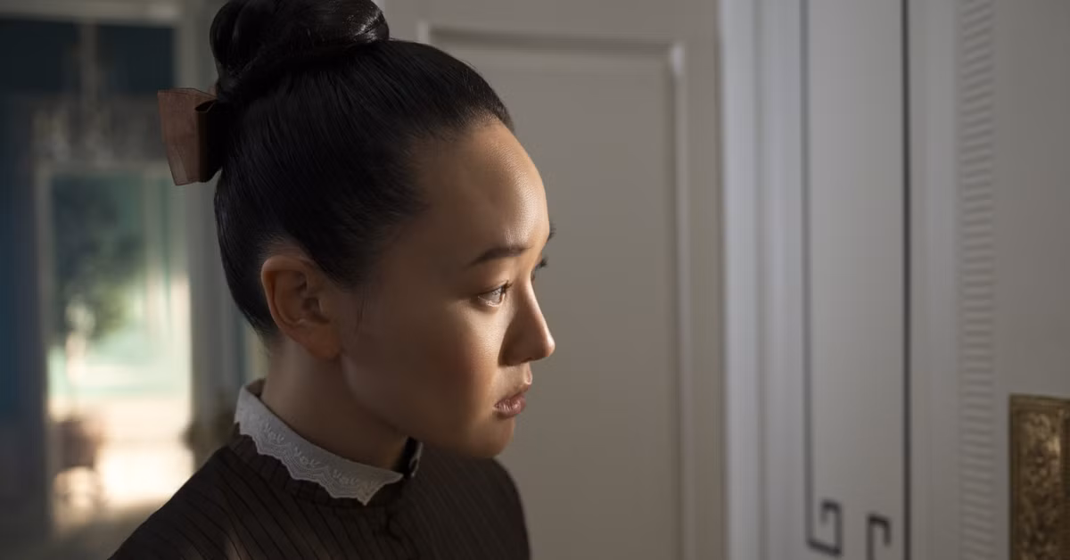 Sophie Baek standing outside of the door to the Penwood sitting room. She is in her maid attire, looking longingly through a crack in the door.