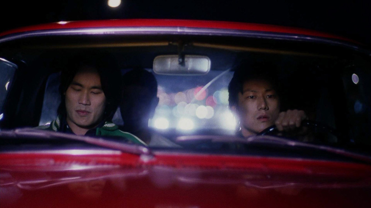 A still of Daric, portrayed by Roger Fan, and Han, portrayed by Sung Kang, in Han's red car, both with vaguely uncomfortable expressions.